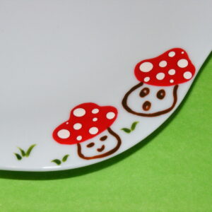 Détail petite assiette plate forme fleur en porcelaine blanche peinte à la main, décors champignons rigolos